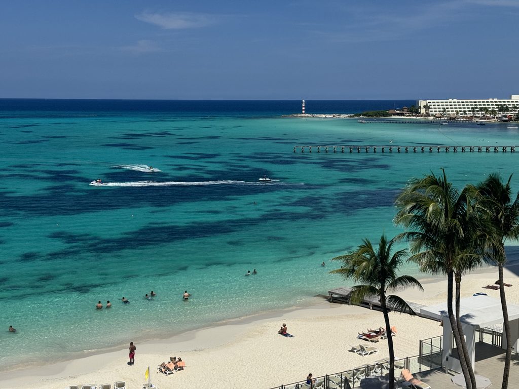Tropical beach view from a balcony with palm trees and clear blue water.